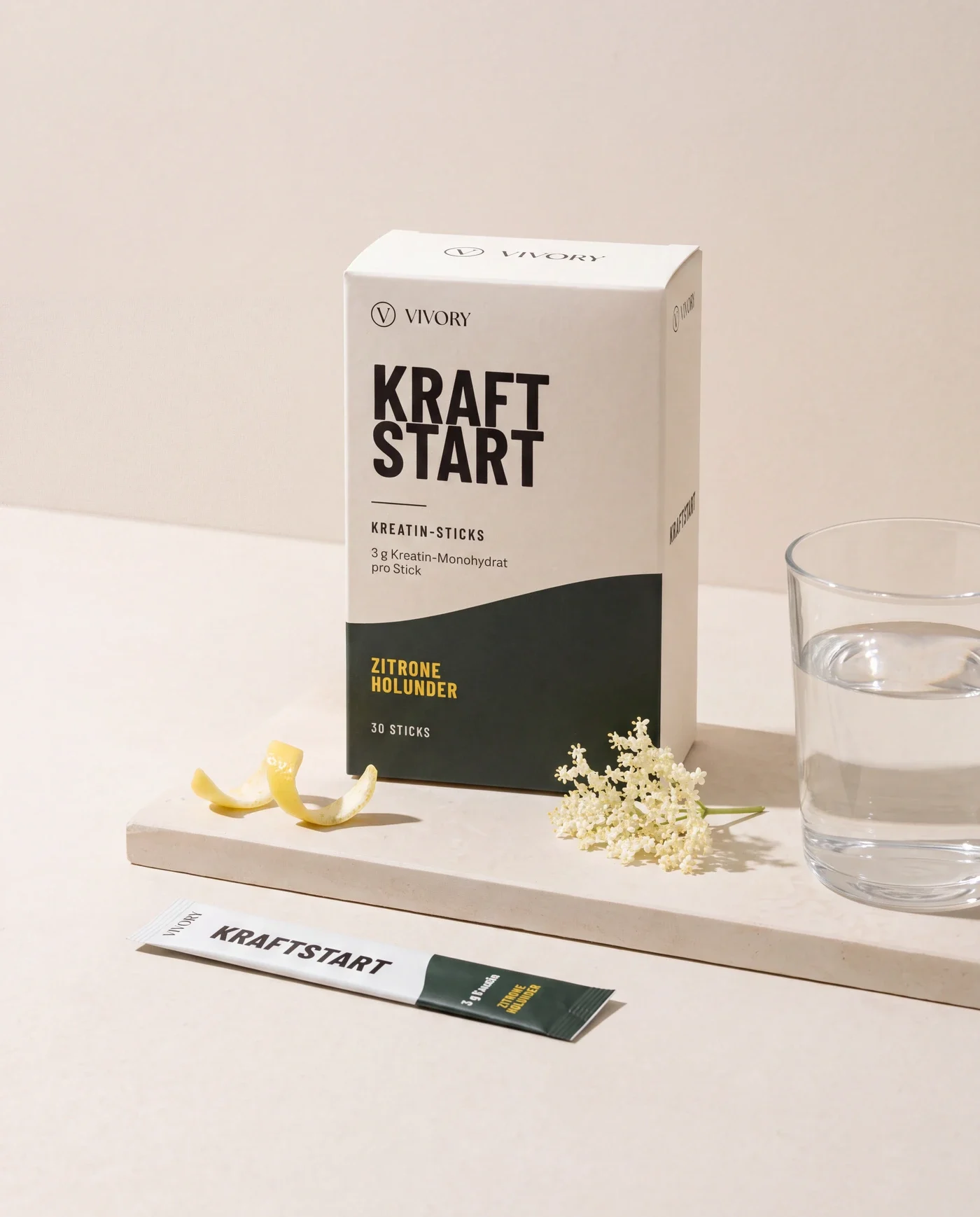 Konzeptvisualisierung: Verpackung und ein Stick VIVORY Kraftstart neben einem Glas Wasser, Zitronenschale und Holunderblüten
